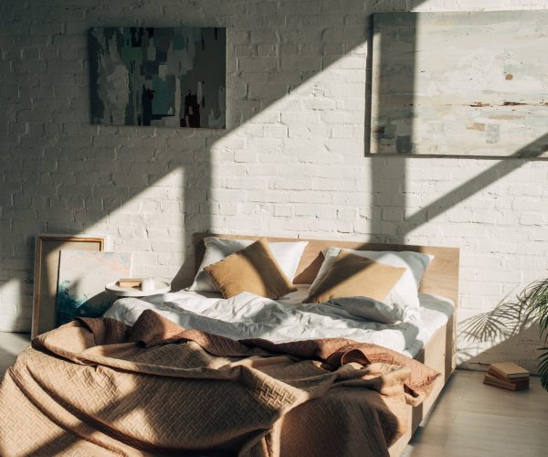 bedroom interior with bed, pillows and paintings in sunlight with shadows